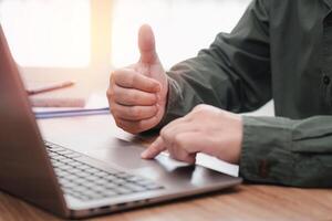 Business man thumbs up for work on the project successfully using computer and writing on a paper on desk in office photo