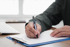 A man use a pen writing on the white paper clip board file and keyboard smartphone on table in work office photo