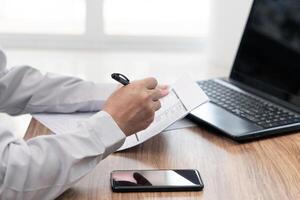 A man use pen write on the checklist paper in office with repair work of car and laptop computer smartphone on wood table photo