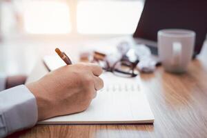 A man use pencil write on notebook paper and crumple paper laptop computer glasses coffee cup on table for office work photo