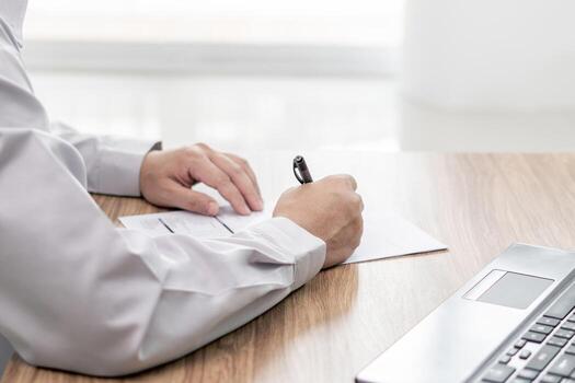 A man write on document on table and use laptop working online check part list in service center office photo