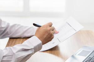 A man use pen write on the checklist paper check service list in office with repair part of car and laptop computer on wood table photo
