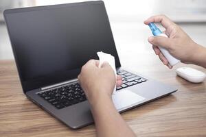 Close up hand a man use white cloth clean laptop display alcohol bottle spray in hand cleaning and primary disease prevention in home concept photo