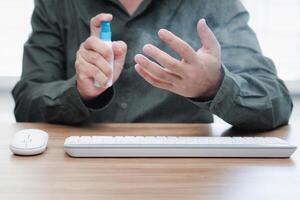 Close up hand a man use alcohol bottle spray clean hand and keyboard mouse desktop on the table primary disease prevention in home concept photo