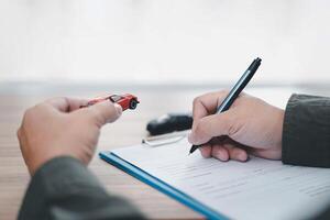 Car insurance concept Man use pen write insurance documents on wood table and a toy car model in hand photo