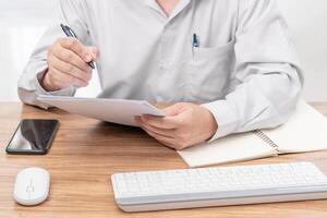 A man write on the paper check service list in office with repair part of car and laptop computer smartphone mouse keyboard on wood table photo