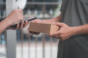 Delivery man and women appending signature in digital mobile phone after receiving parcel from courier at home photo