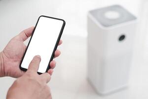 Close up hand a man holding smartphone with white screen display and online connect to air purifier using technology to control health equipment anywhere via the Internet photo