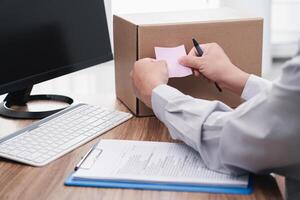 Close up hand a man paste the pink note paper on the side of the box to mark it and checklist credit card and use computer desktop for stock check photo