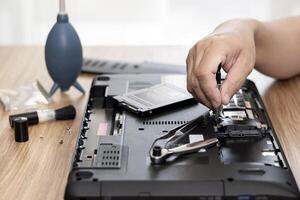 Computer repair men hands use screwdriver remove nut of hard disk of laptop for check and repair and computer repair tools on table photo