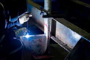 The welder is repairing the surface of the iron steel part in mix welding process in factory photo