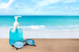 Alcohol gel in clear plastic Pump type bottles and clear glasses on the wood table and sea with blue sky background,safety summer concept in travel photo