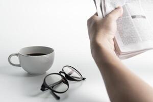 White coffee cup,glasses,and a man read News paper on the white table photo