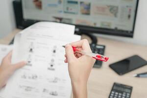 profesor utilizar un rojo bolígrafo cheque ejemplo sábana y examen equipo en el madera mesa y utilizar escritorio computadora trabajando en el antecedentes foto