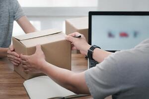 Parcel receiving officer man hold Parcel box from women and use laptop to register in the online system to send parcels to the destination correctly transportation system concept photo