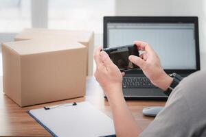 Close up hand a man use smartphone take photo parcel box  to store information and use laptop to register in the online system