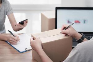 Parcel man use a pen marking address on Parcel box and women Sign documents in paper Sign document and check online system to send parcels in smartphone delivery concept work photo