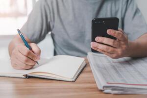 Man use mobile phone search news information from internet and write on notebook and newspaper on wood table search information during an epidemic photo