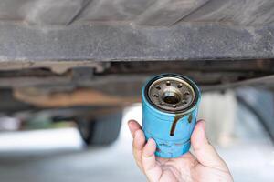 Close up hand a man hold old oil filter and remove from under car on lift for car maintenance concept photo