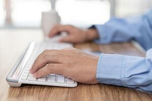 Hand a man typing on computer desktop keyboard mouse and coffee cup on table in working photo