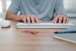 un hombre utilizar ratón escritorio computadora y teclado con crédito tarjeta bolígrafo y Nota libro en mesa trabajando a hogar concepto foto