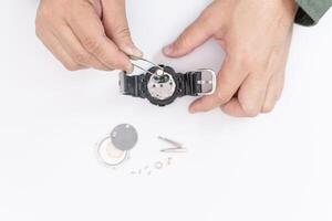 A man use pliers to clamp the digital watch battery remove and change in repairing broken wristwatches on white table photo