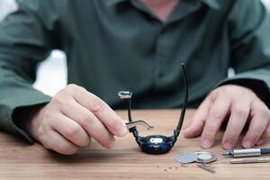 un hombre usa alicates para sujetar la batería del reloj digital, quitarla y cambiarla para reparar relojes de pulsera rotos y herramientas en una mesa de madera foto