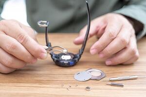 un hombre usa alicates para sujetar la batería del reloj digital, quitarla y cambiarla para reparar relojes de pulsera rotos en una mesa blanca foto