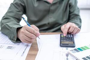 Engineering work concept Close up hand a man use pencil and calculator in Calculating drawing and document on the wood table photo