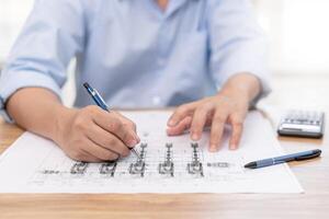 Engineering work concept Close up hand a use pencil mark CAD drawing and calculator in Calculating document on the wood table photo