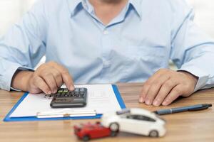 coche seguro concepto un hombre utilizar calculadora en mesa a calcular el dañar desde un coche accidente y coche modelo accidente concepto en madera mesa foto