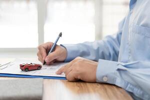 Car insurance concept Man holding a accident toy car and write insurance documents on wood table photo