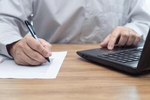 Man use pen write on a graph paper in work process everyday on table and use laptop computer in background photo
