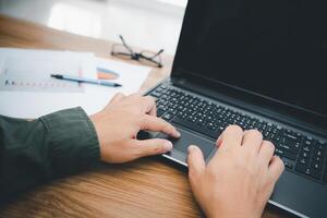A man touch the mouse pad of laptop computer and typing on the keyboard in business work on the wood table photo