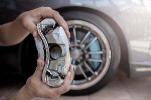 Car service run stop system concept close up caliper brake of car in hand a man and wheel of car in background photo
