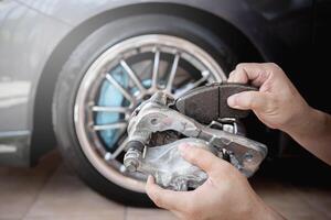 Service concept photo of brake system Close up hand a man hold brake pad in put to caliper and wheel car in background