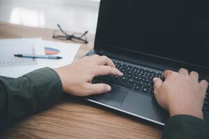 A man touch the mouse pad of laptop computer and typing on the keyboard in business work on the wood table photo