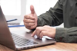 Business man thumbs up for work on the project successfully using computer and writing on a paper on desk in office photo