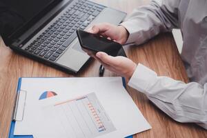 Business man use smartphone analyzing business work on document data graph with laptop computer calculate for new project of business strategy at workplace photo