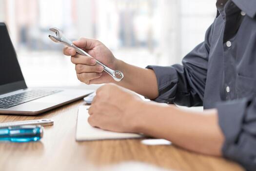 el técnico sostener un llave inglesa en mano y usado un computadora ordenador portátil a analizar el roto de coche en Servicio habitación concepto foto