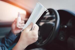 cerca arriba mano un hombre sostener máscara y alcohol rociar para evitar gérmenes y virus en cada día y en lado coche en antecedentes foto