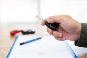 Close up hand of man holding and push remote control for lock and Un-lock car and insurance document on table concept model toy a car in blur background photo