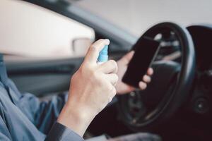 A man spray alcohol onto your smartphone after use to prevent germs and viruses in every day and in side car in background photo