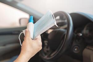 Close up hand a man hold mask and Alcohol spray for prevent germs and viruses in every day and in side car in background photo