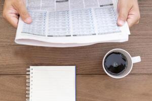 Coffee cup notebook paper on vintage wood table with a man read newspaper in coffee time photo