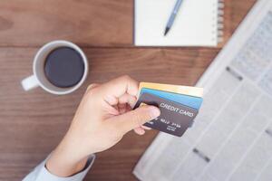 Hand a man hold credit card for pay and reading newspapers in coffee time with pen note book coffee cup on wood table photo