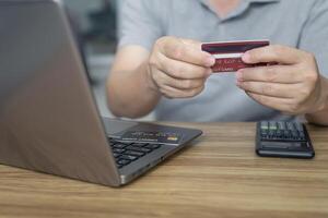 A man hold credit card in hand check number on card and input in laptop computer and calculator on wood table for shopping online order home shopping and delivery concept photo