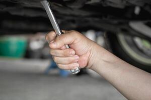 Close up wrench in hand a man removing a nut of car oil pan To change the oil in the check period photo