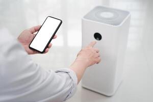 Close up hand a man holding smartphone with white screen display and online connect to air purifier using technology to control health equipment anywhere via the Internet photo