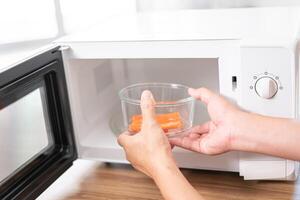 Close up hand a man putting glass bowl with crab sticks in microwave oven to cook in the kitchen photo